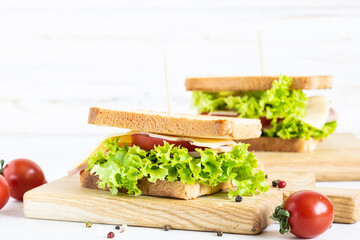 Fresh homemade sandwiches with ham, tomatoes, cheese and salad leaves on white wooden background. Breakfast idea.