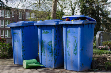 drei große blaue Mülltonnen auf einem Friedhof in Deutschland