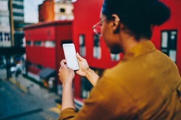 Selective focus on modern smartphone with mock up screen, rear view of dark skinned hipster girl holding mobile phone connected to 4G for chatting and blogging in social networks. Copy space screen