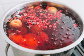 Fresh fruits are boiled in boiling water in a metal pan on the stove. Delicious stewed apricot, apples, cherries, raspberries. Photography, concept.
