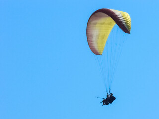 Silhouette of paragliding tandem floating in the air against clear blue sky. active lifestyle and extreme sport adventure concept. People on paraplane flying in blue sky