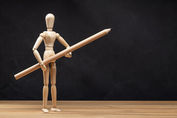 Wooden mannequin holding a pencil. Blackboard background. Drawing concept. Copy space