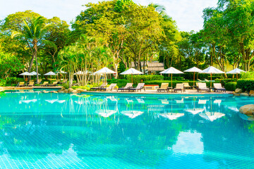 Beautiful luxury umbrella and chair around outdoor swimming pool in hotel and resort with coconut palm tree on blue sky