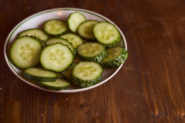 Fresh cucumbers lie in white saucers on a brown background
