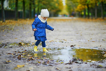 Child wearing yellow rain boots and jumping in puddle on a fall day