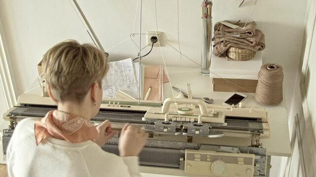 A woman works behind a knitting machine view from back