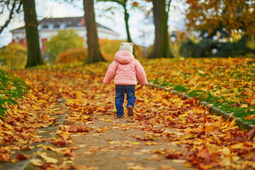 Adorable cheerful toddler girl running in Montsouris park in Paris