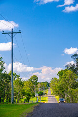 Car on asphalt country road (Schilling Road, Calliope) in queensland, with telephone poles and lines running alongside