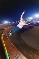A young skateboarder rides at speed sideways along the ramp by spreading his hands to the sides. Night shot with long exposure at night speed in a skatepark © yanik88