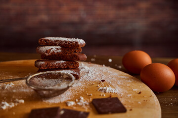 Chocolate cakes sprinkled with powdered sugar on a wooden table. next to it are eggs and pieces of chocolate. blurred background