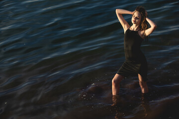 Fototapeta premium girl in a black dress in blue water posing evening time