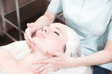 Fototapeta na wymiar A professional female massage therapist does a facial massage to a client in a spa facial care salon. The concept of facial massage and skin care