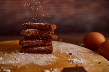 Chocolate cakes sprinkled with powdered sugar on a wooden table. next to it are eggs and pieces of chocolate. blurred background