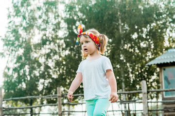 surprised emotional sweet pretty child, girl sitting on a fence in the village. Beautiful curly girl walks in the countryside. farming.nature and ecology in the country. outdors