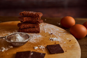 Chocolate cakes sprinkled with powdered sugar on a wooden table. next to it are eggs and pieces of chocolate. blurred background