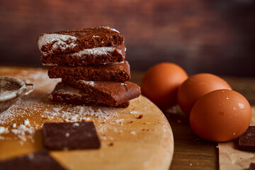 Chocolate cakes stacked on a wooden table. next to it are eggs and pieces of chocolate. blurred background