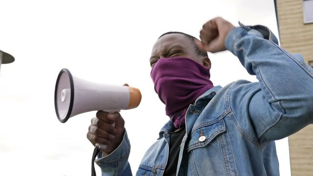 At a protest against racism dark-skinned young protester shouts angrily in megaphone. BLM.