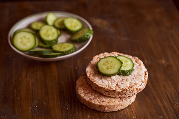 round buckwheat bread on which are two fresh cucumbers on a brown background