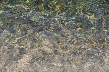 Abstract natural colorful background. Shallow water on a pebble sea beach on a calm sunny day