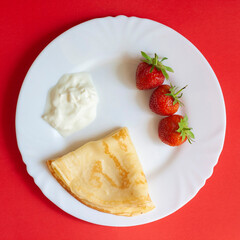 Breakfast, strawberries, pancakes and cream on a white plate
