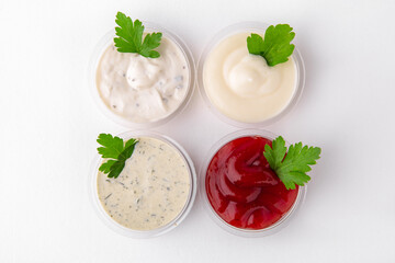 Assorted different sauces in plastic: ketchup, mustard, sour cream. Topping for dishes for delivery. Isolated on a white background.