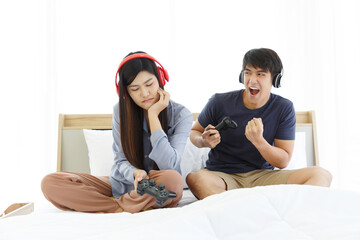 Obraz na płótnie Canvas Young Asian Lovely Couple Playing Video Game console on bed in Bedroom. Spends time together. White Background. Male and Female. Bored Girl Friend.