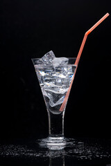 Clear drinking glass with ice and a orange plastic straw.