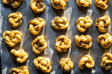 Unbaked cinnamon knots on baking paper on baking tray.