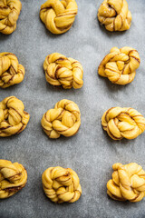 Unbaked cinnamon knots on baking paper on baking tray.