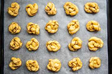 Unbaked cinnamon knots on baking paper on baking tray.