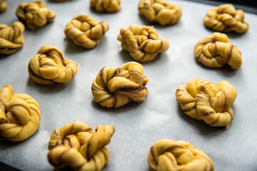 Unbaked cinnamon knots on baking paper on baking tray.
