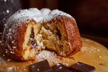 Cut homemade cupcake with chocolate cream inside sprinkled with powdered sugar on a wooden board. Close-up.