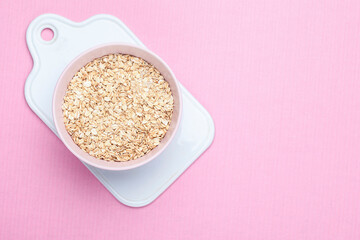 A bowl of dry oatmeal on a pink background with copy space for text. Cooking oats porridge concept. Flat lay