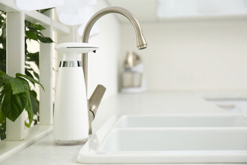 Modern automatic soap dispenser near sink in kitchen. Space for text