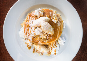 Three pancakes, caramel, almond flakes, Italian meringue, vanilla cream, powdered sugar on a white plate. Top view.