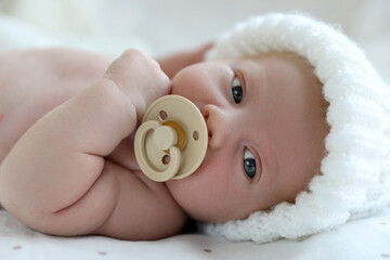 Cute newborn baby in white knitted hat lying on bed, closeup
