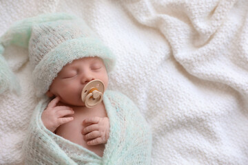 Cute newborn baby in warm hat sleeping on white plaid, top view. Space for text