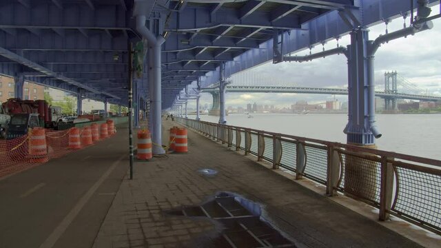 POV walk under FDR Drive structure, New York City skyline cloudy sky, Manhattan Bridge view