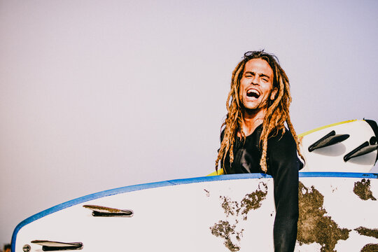 a smiling surfer with dreadlocks in a sunny beach - Powered by Adobe