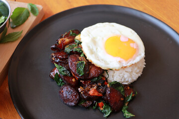 Chinese sausage fried with basil and fried egg with rice in the black round dish, with cooking ingredients.
