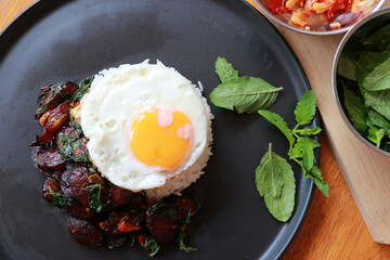 Chinese sausage fried with basil and fried egg with rice in the black round dish, with cooking ingredients.