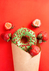 donut with green glaze and red sprinkles, fresh strawberries in an envelope on a red