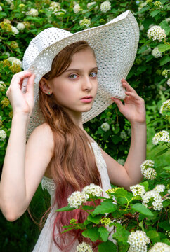 Portrait White Girl 11 Years Old In A White Dress And Hat In A Blooming Garden