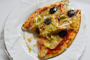 Pizza leftovers on a plate covered with plastic wrap