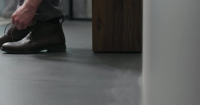Slow motion dolly shot of young man lace up his brown leather chukka boots indoor