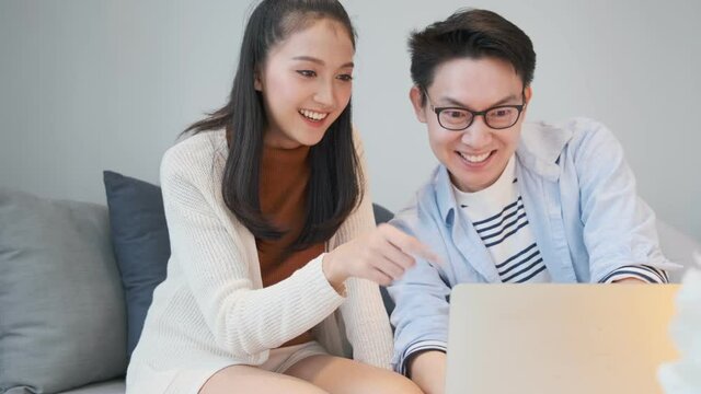 attractive lovely asian marry couple enjoy watch online movie from laptop new normal lifestyle on sofa couch in living room home interior background