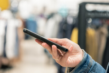 A mobile phone in buyer hand close up on a clothing store background.
