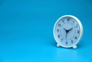 Selective focus of white table clock isolated on a blue background with a copy space.