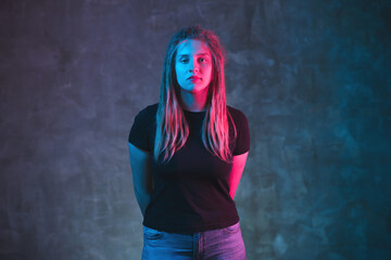 Young woman with dreadlocks in colorful neon lighting on dark background. Stylish girl in futuristic environment.