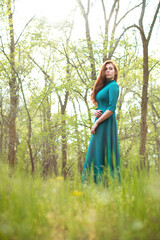 Beautiful woman in elegant dress stands in forest on background of green trees. Natural beauty concept.